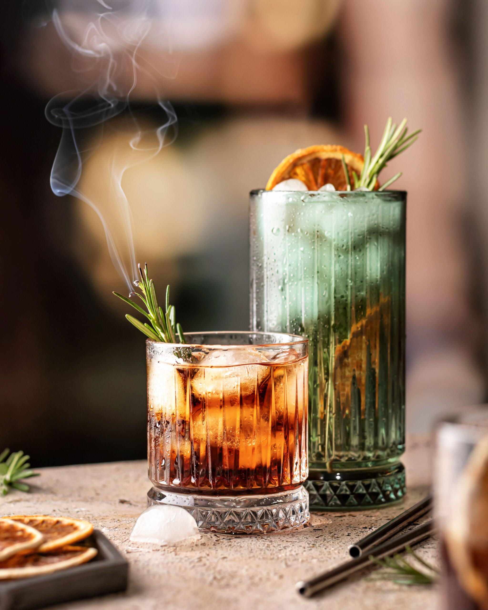 Cocktails on the bar. Whiskey-cola, cuba libre iced cocktails with rosemary and dried orange slices with metal straws behind.