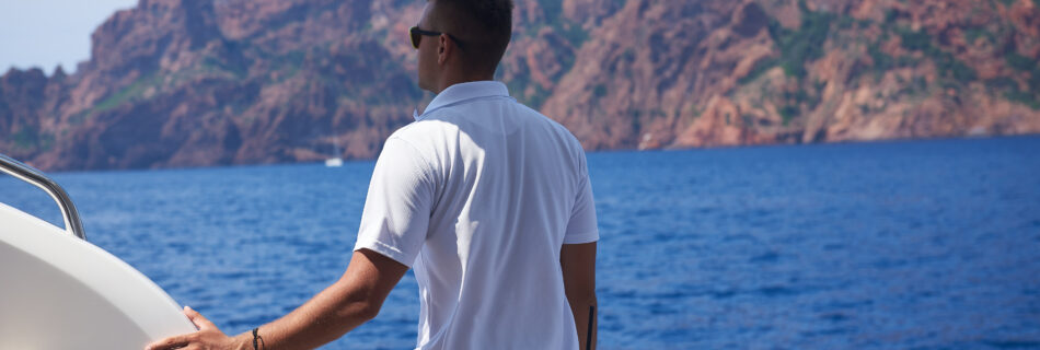 Deckhand enjoying scenic ocean view from yacht with rocky mountain backdrop