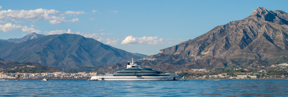 starboard side of a luxury mega yacht of more than 100 meters docked outside of puerto banus. landscape with the iconic mountains of marbella